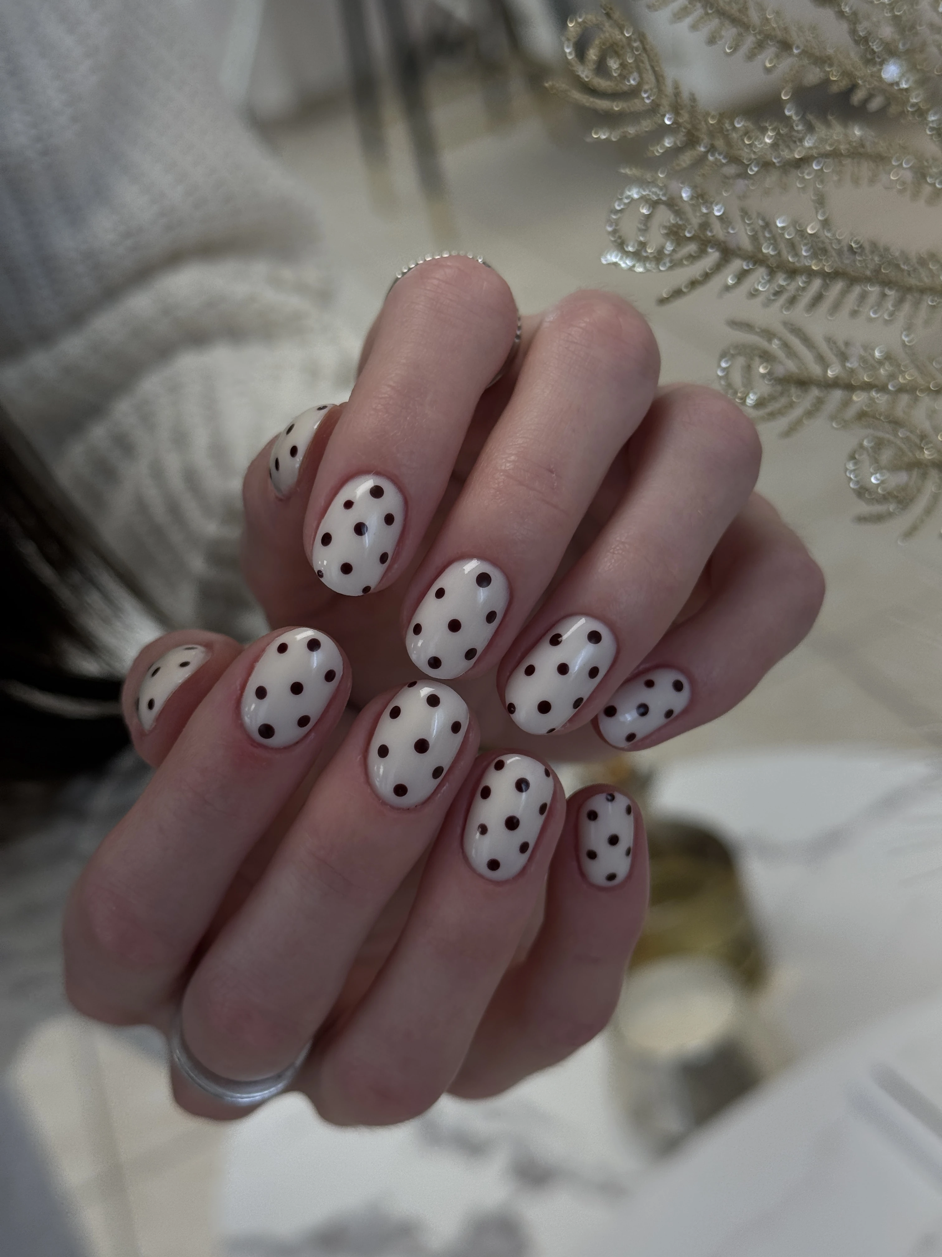 Mississauga nail art with dark polka dots on creamy off-white oval nails, fingers interlaced in a white sweater.
