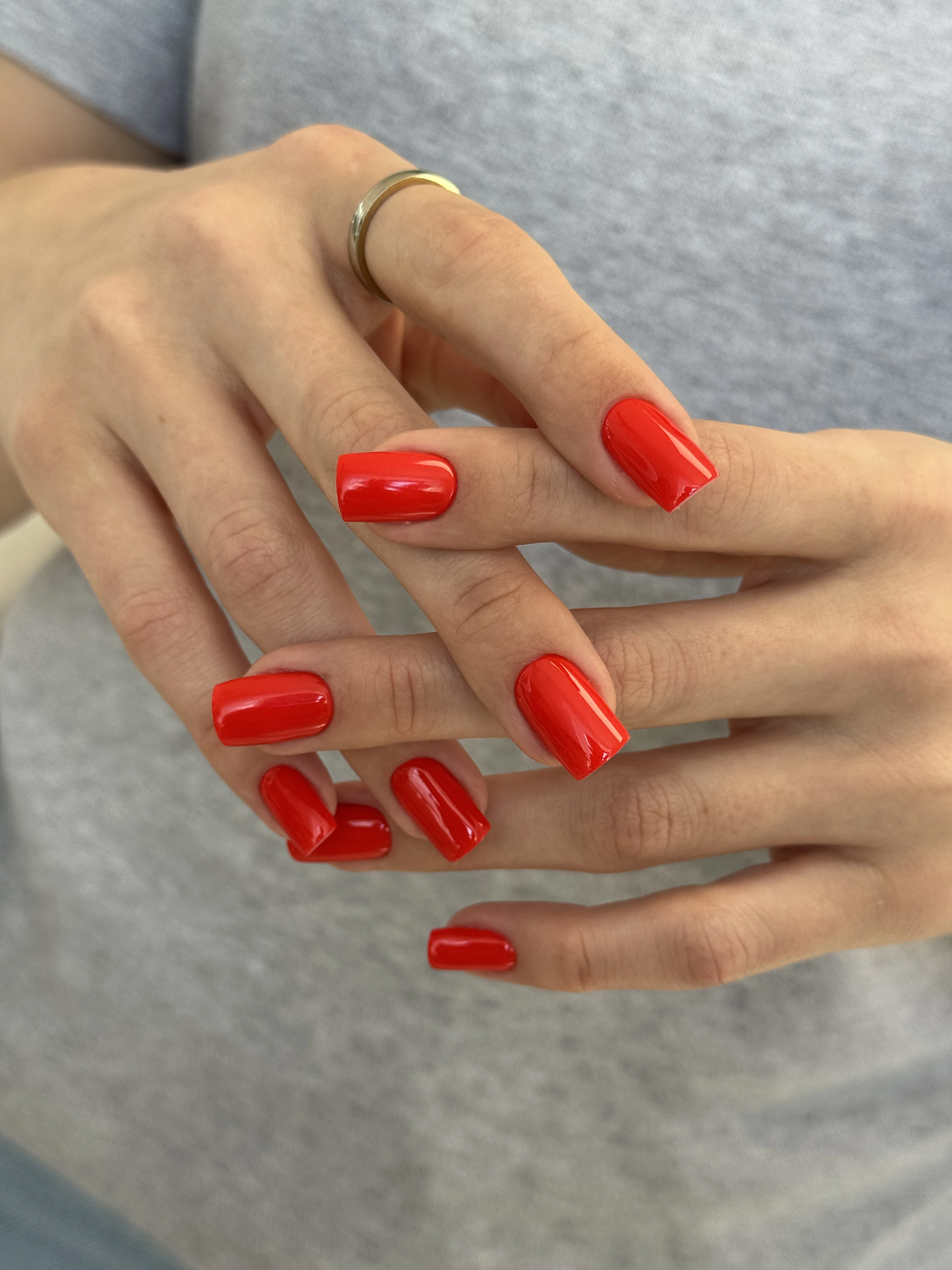 Glossy cherry-red gel polish on medium squoval nails with a gold band ring, a bold look from My Beauty Space Mississauga.