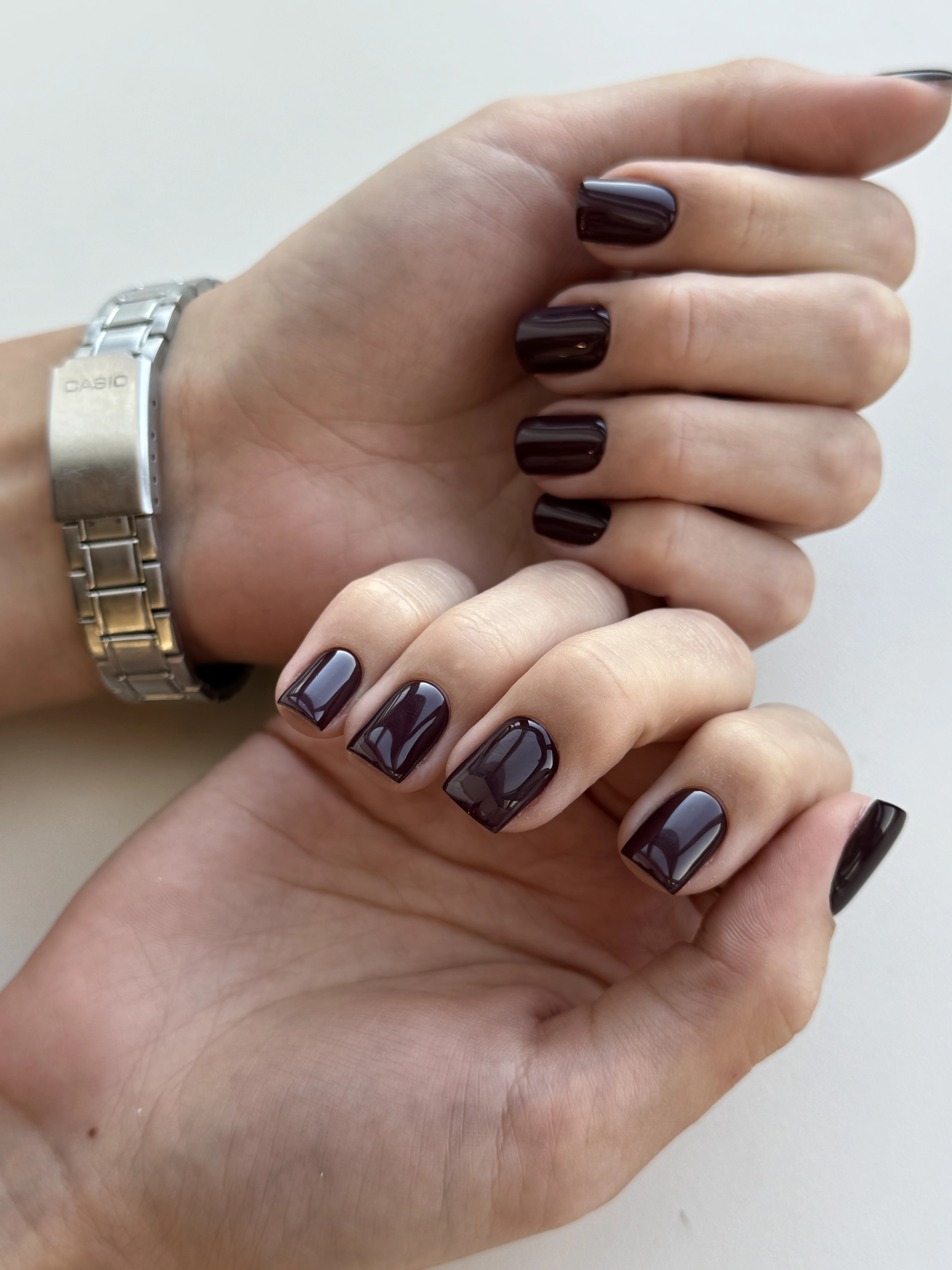 Dark plum hard gel on short square nails beside a silver Casio watch, a rich finish from My Beauty Space Mississauga.