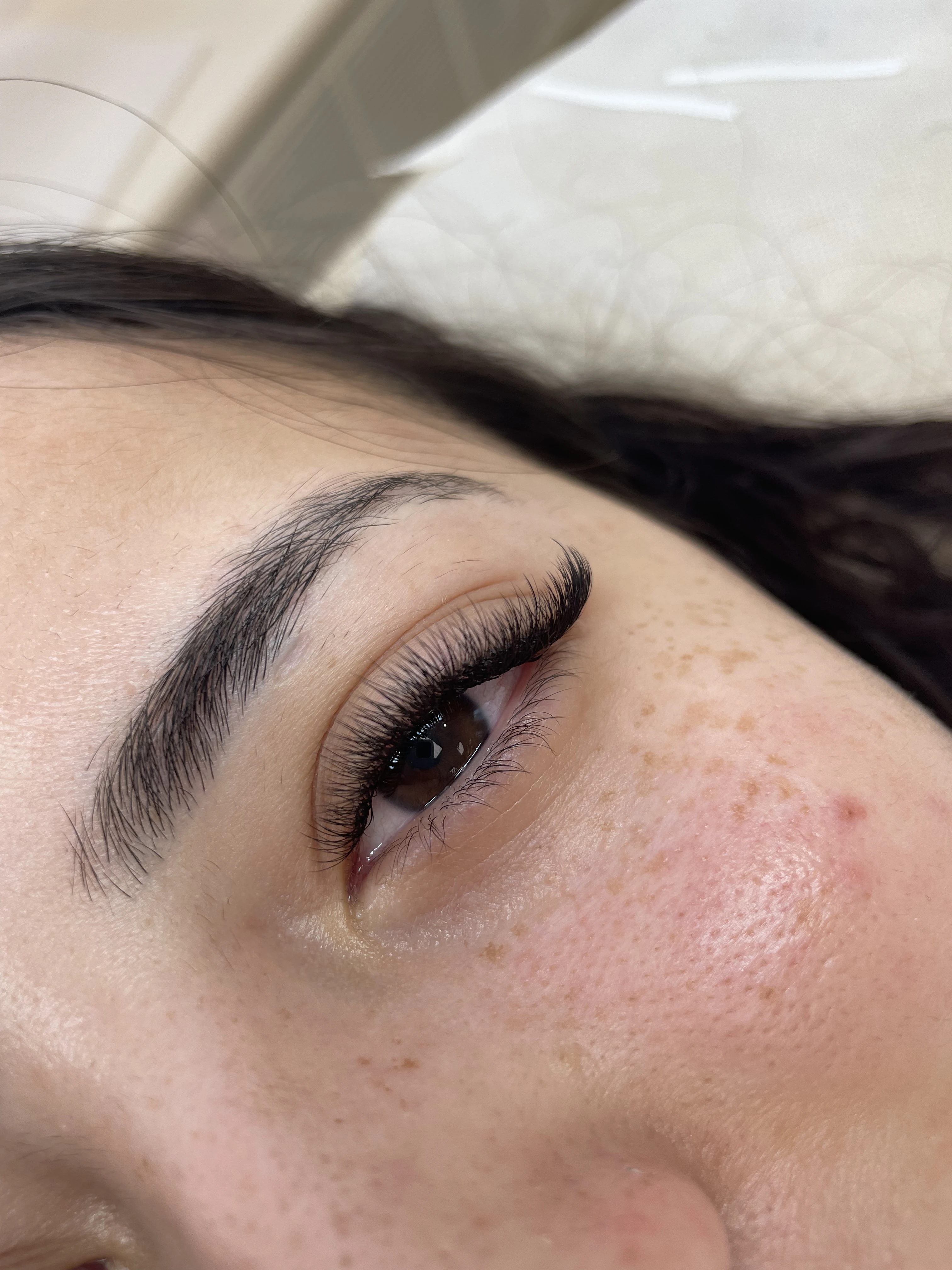 Top-down view of freckled skin with uniform 3D volume lash fringe on a salon bed at My Beauty Space Mississauga.