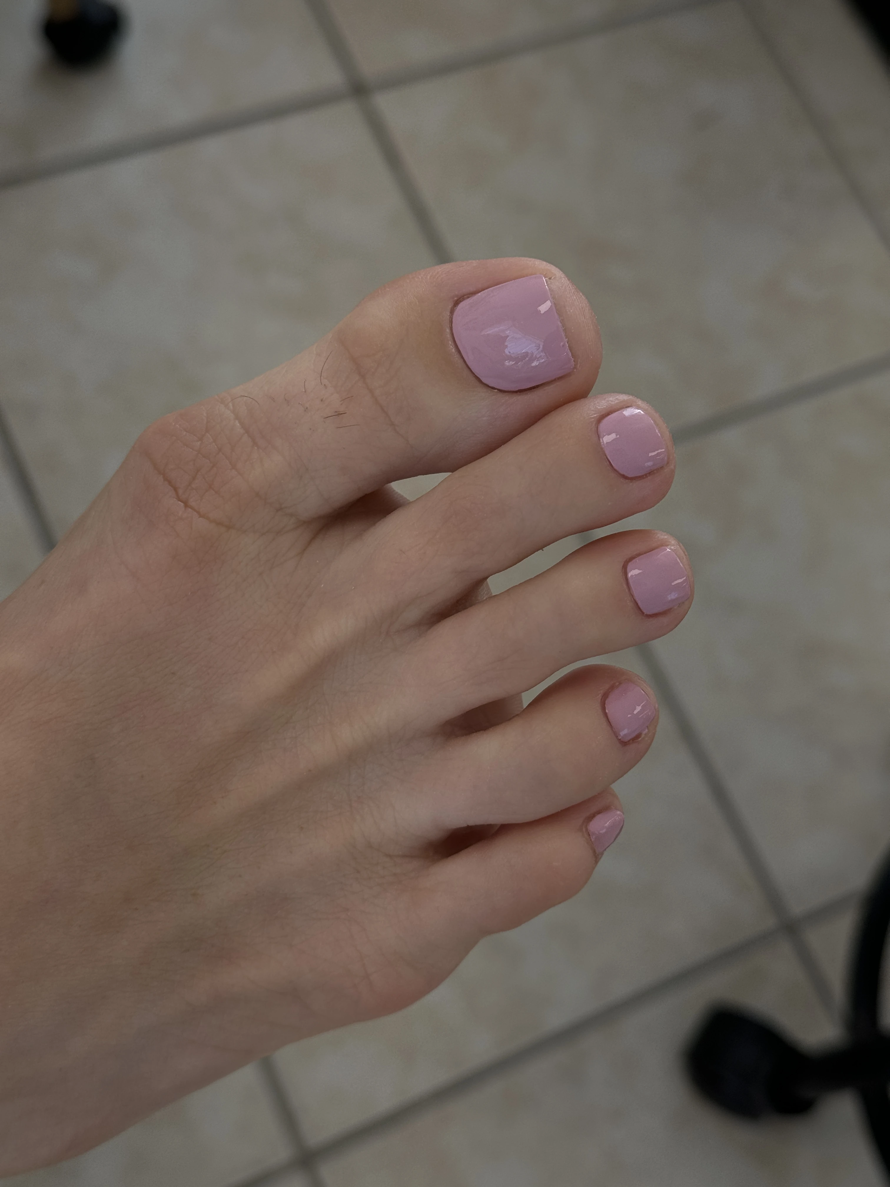 Mississauga pedicure with dusty mauve-pink regular polish on short square toes, foot angled over tiled salon flooring.