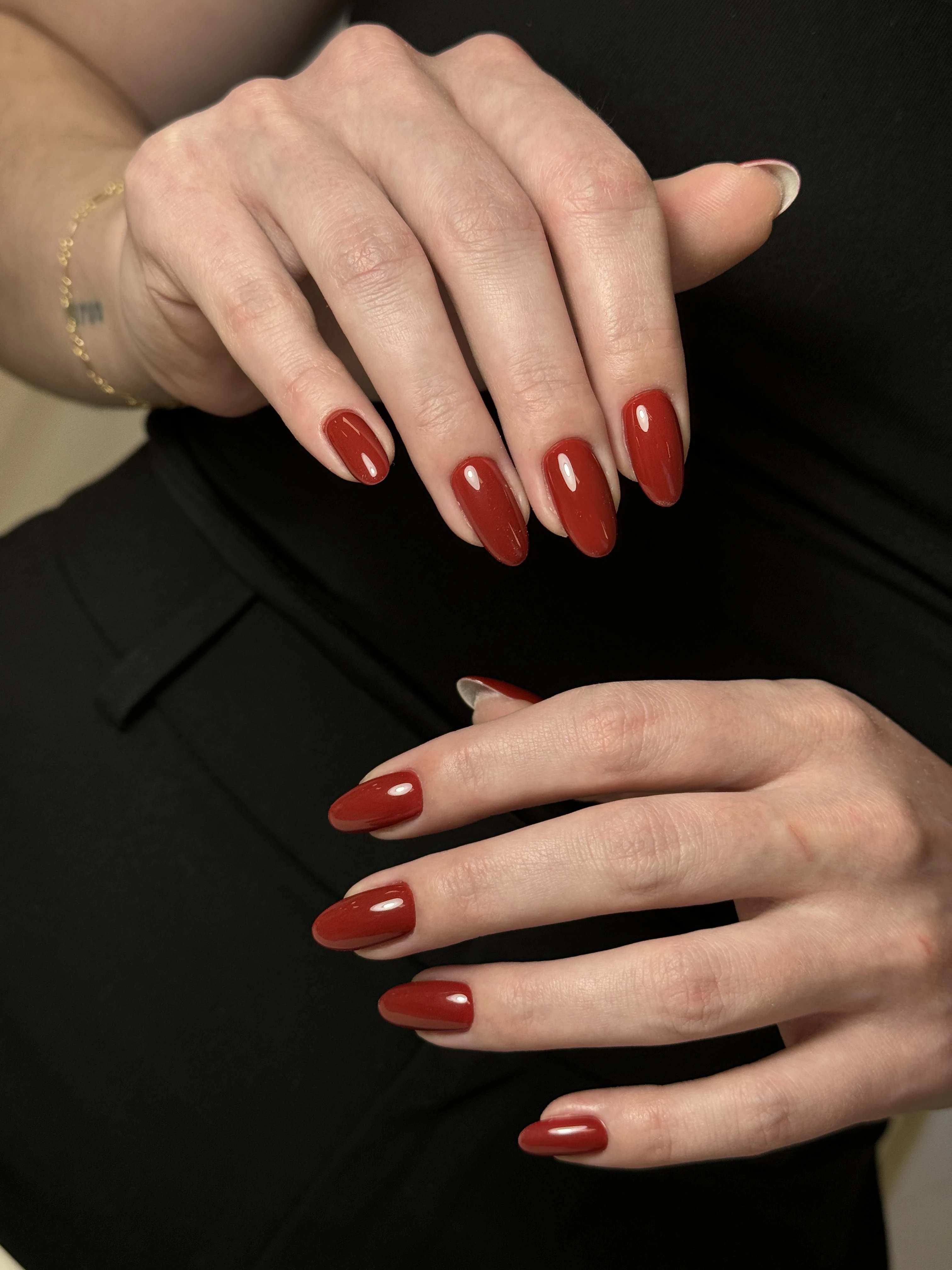 Glossy terracotta-red hard gel on almond nails with a gold chain bracelet, styled at My Beauty Space in Mississauga.