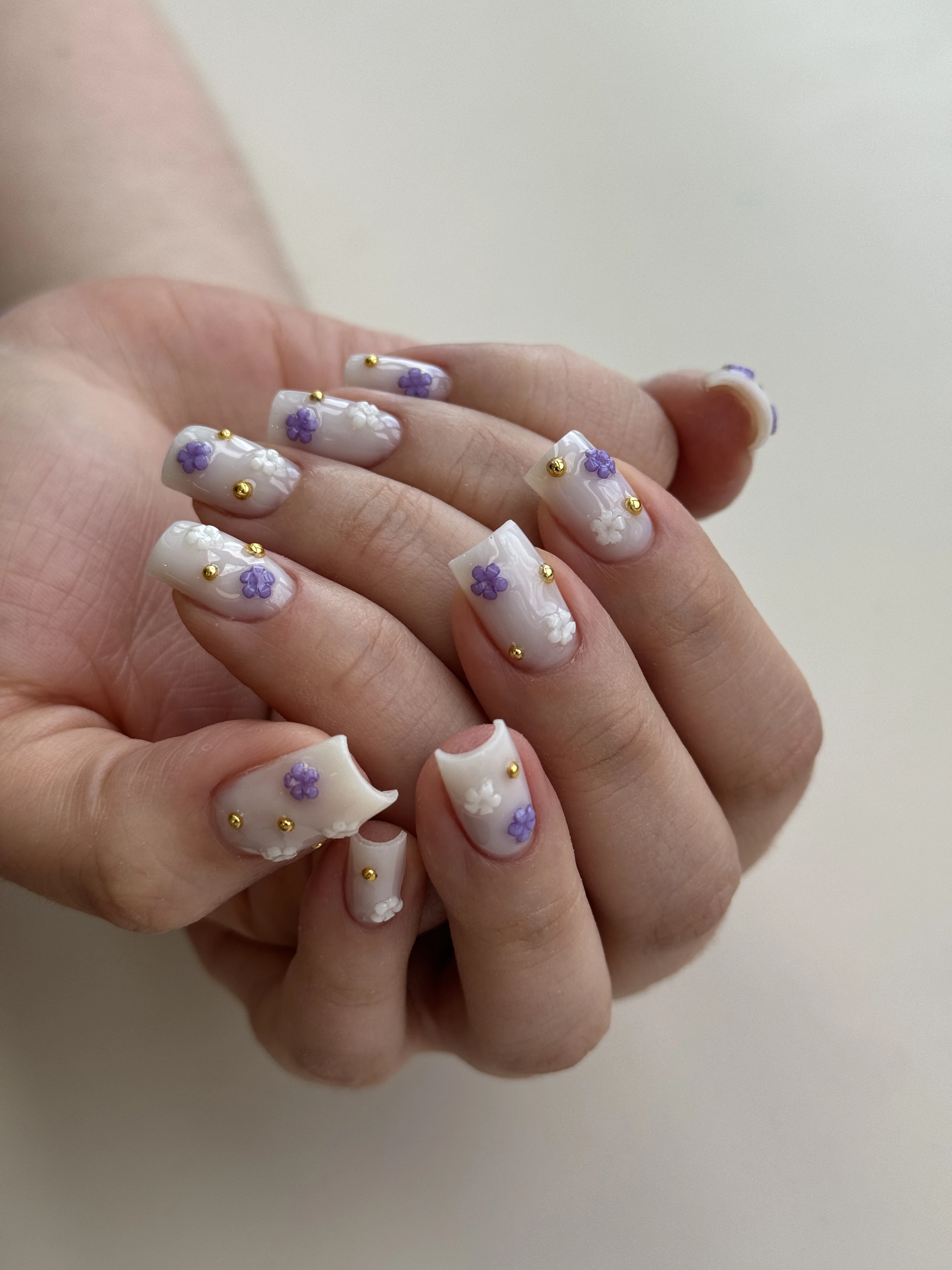 Milky marble Gel-X nail design at My Beauty Space with 3D white-purple florals and gold studs on square extensions.